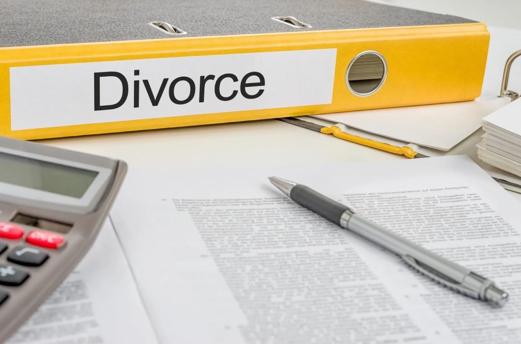 Large yellow binder labeled “Divorce” resting on table with documents, ballpoint pen, and calculator.