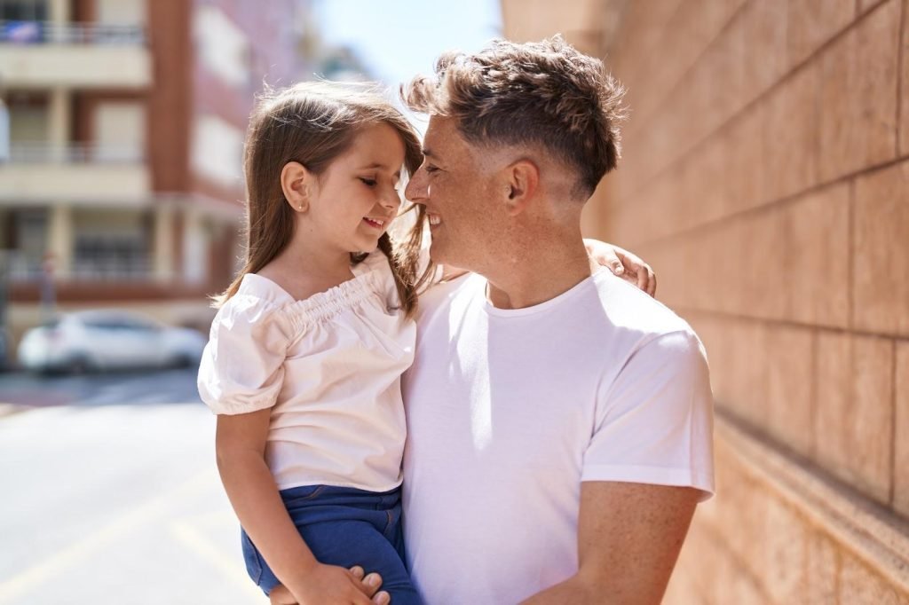 A father and daughter hug and smile on a sunny city street.
