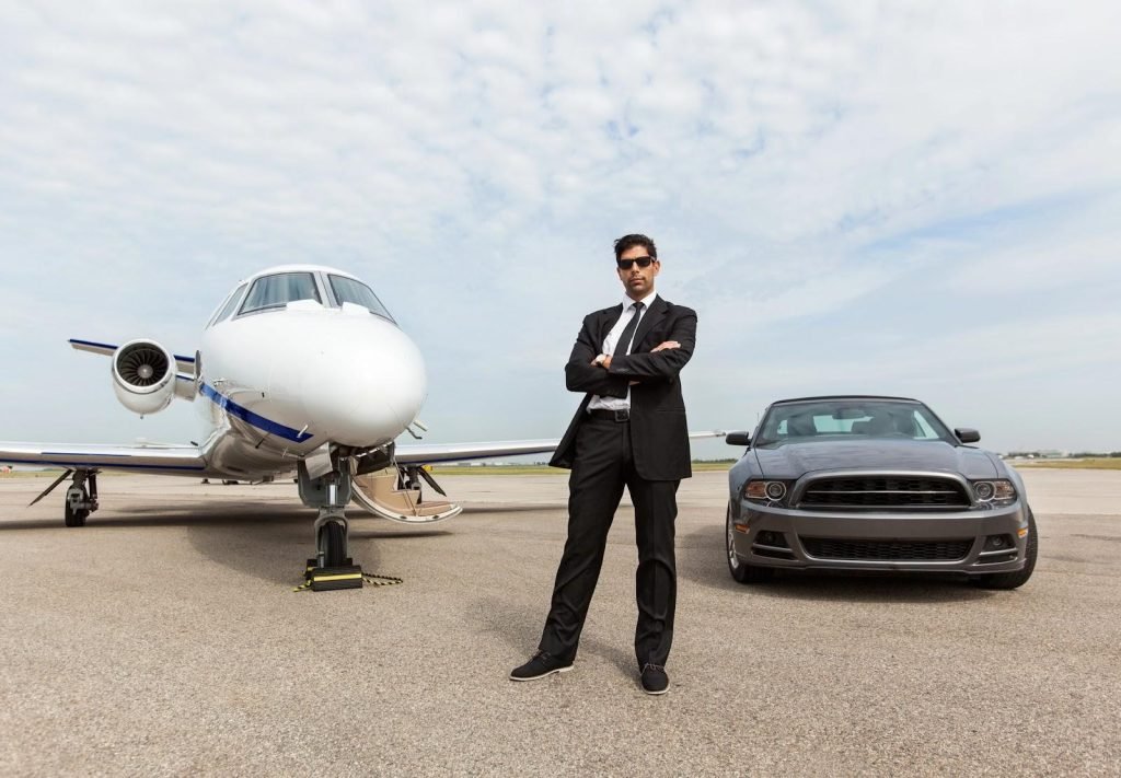 A wealthy businessman stands in front of his private plane and expensive car, which may be community property in his high net worth divorce.