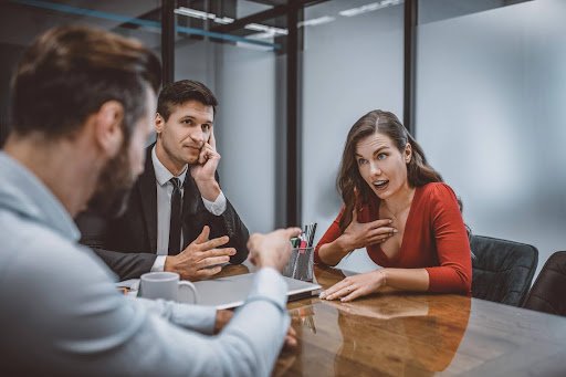 Spouses arguing across a conference table during divorce mediation while the mediator looks on; alternative dispute resolution for family law cases.
